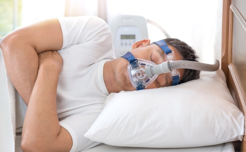 man lying on his side wearing cpap machine on face for sleep apnea treatment