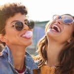 friends enjoying outdoor street. Brazilian girl laughing and blowing chewing gum with friend embracing her.