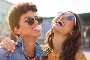 friends enjoying outdoor street. Brazilian girl laughing and blowing chewing gum with friend embracing her.