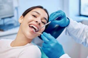 Latina woman smiles at the dental office while a dentist checks the condition of her teeth. Examinations and cleanings are important