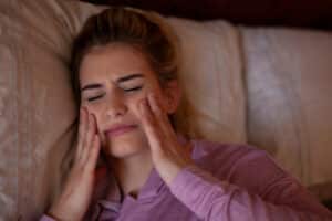 A woman with bruxism holding her cheeks while sleeping