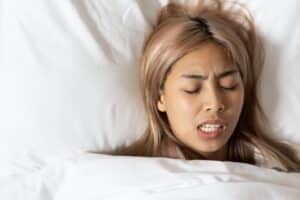A woman with bruxism lying in bed grinding her teeth