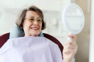 A woman looking in the mirror after getting a dental bridge in Pasadena, TX