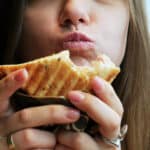 A woman with TMJ disorder eating a sandwich